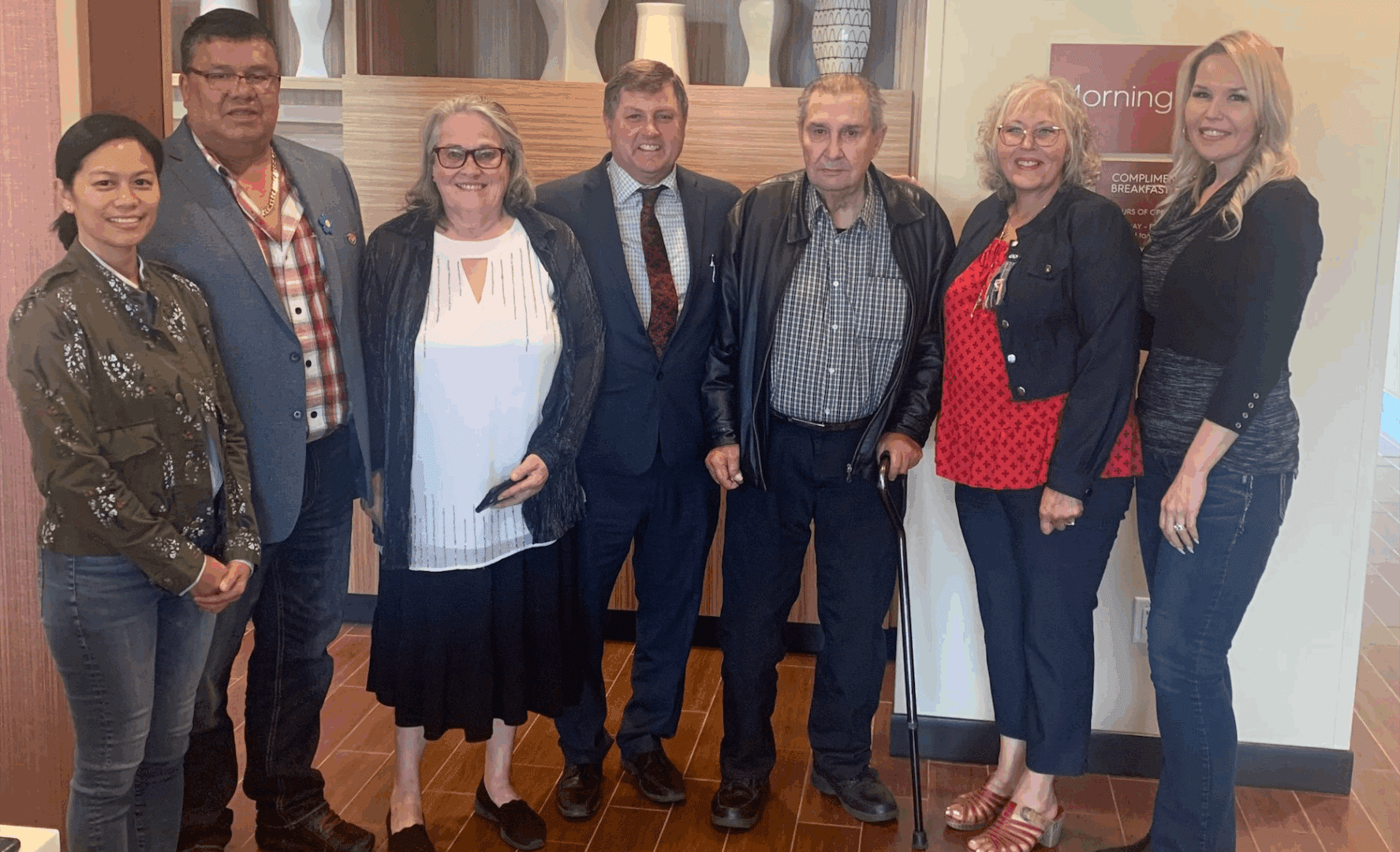 Group of seven people smiling indoors.